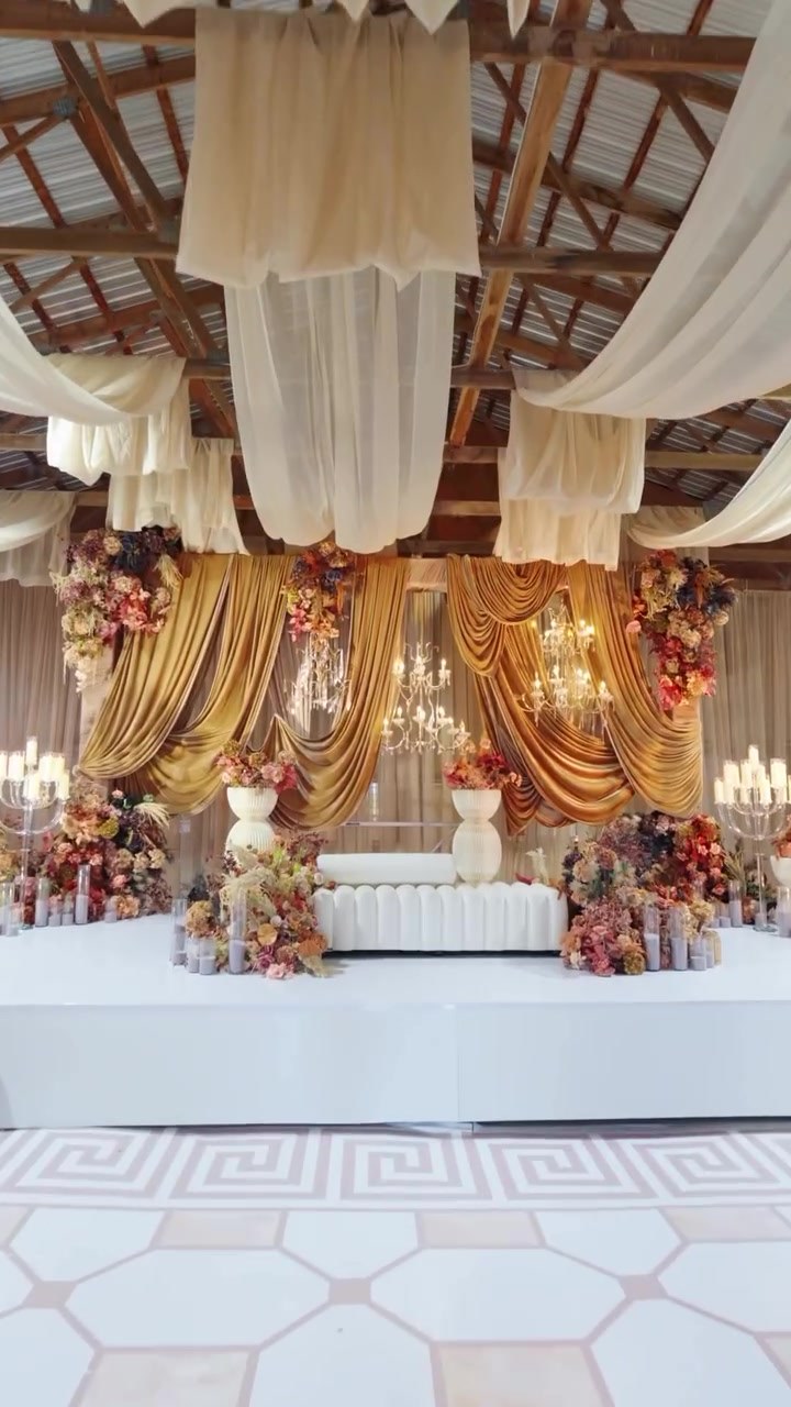 Gold-draped stage with chandeliers and florals at a wedding reception at Amplify Venue near Caledon